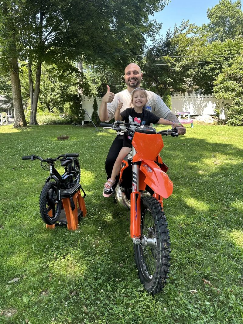 Davin and his daughter giving a thumbs up on his orange dirt bike