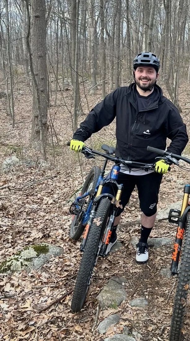 Davin smiling with his mountain bike on a wooded trail